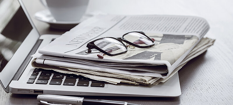 Ein Büro-Arbeitsplatz mit einem Laptop, einer Zeitschrift, einer Brille und einer Kaffeetasse