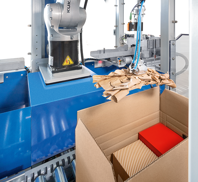 
			Ein Papierpolster wird vollautomatisch in einen Karton mit Versandgütern gelegt.
