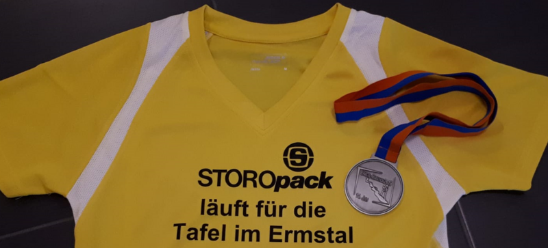 Ein gelbes T-Shirt mit dem Schriftzug „Storopack läuft für die Tafel im Ermstal“ und eine Medaille