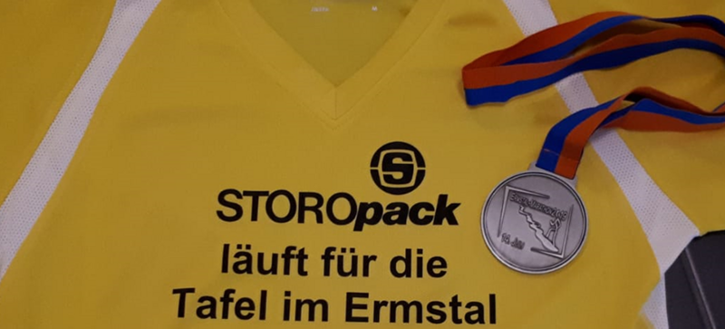 Ein gelbes T-Shirt mit dem Schriftzug „Storopack läuft für die Tafel im Ermstal“ und eine Medaille