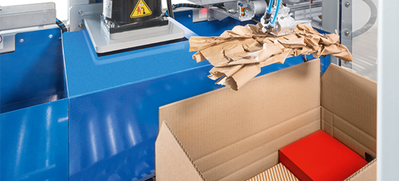 
		  Ein Papierpolster wird vollautomatisch in einen Karton mit Versandgütern gelegt.