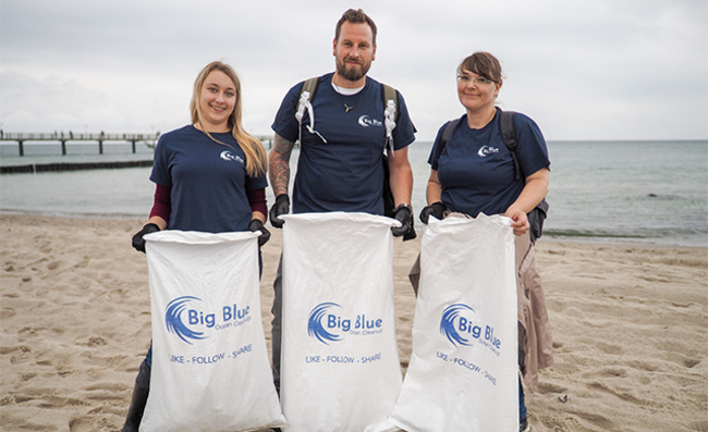 Drei Storopack Mitarbeiter stehen am Strand und halten Müllsäcke