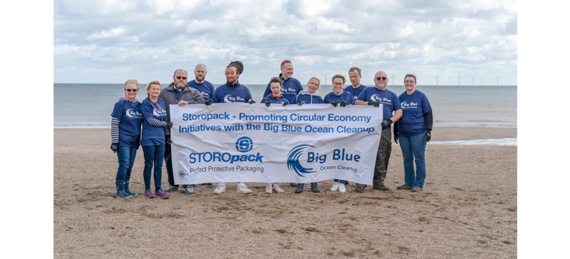Mehrere Menschen sind zu einem Gruppenfoto am Strand aufgestellt und halten einen Banner des Big Blue Ocean Cleanup.